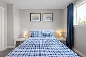 Une chambre à coucher comprenant un lit, deux tables de chevet, deux lampes, une fenêtre avec des rideaux et deux tableaux encadrés accrochés au mur.