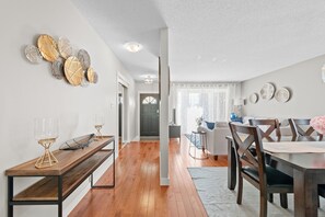 Un espace de repas moderne avec une table et des chaises en bois, un banc avec des verres, et un couloir menant à un espace de vie.