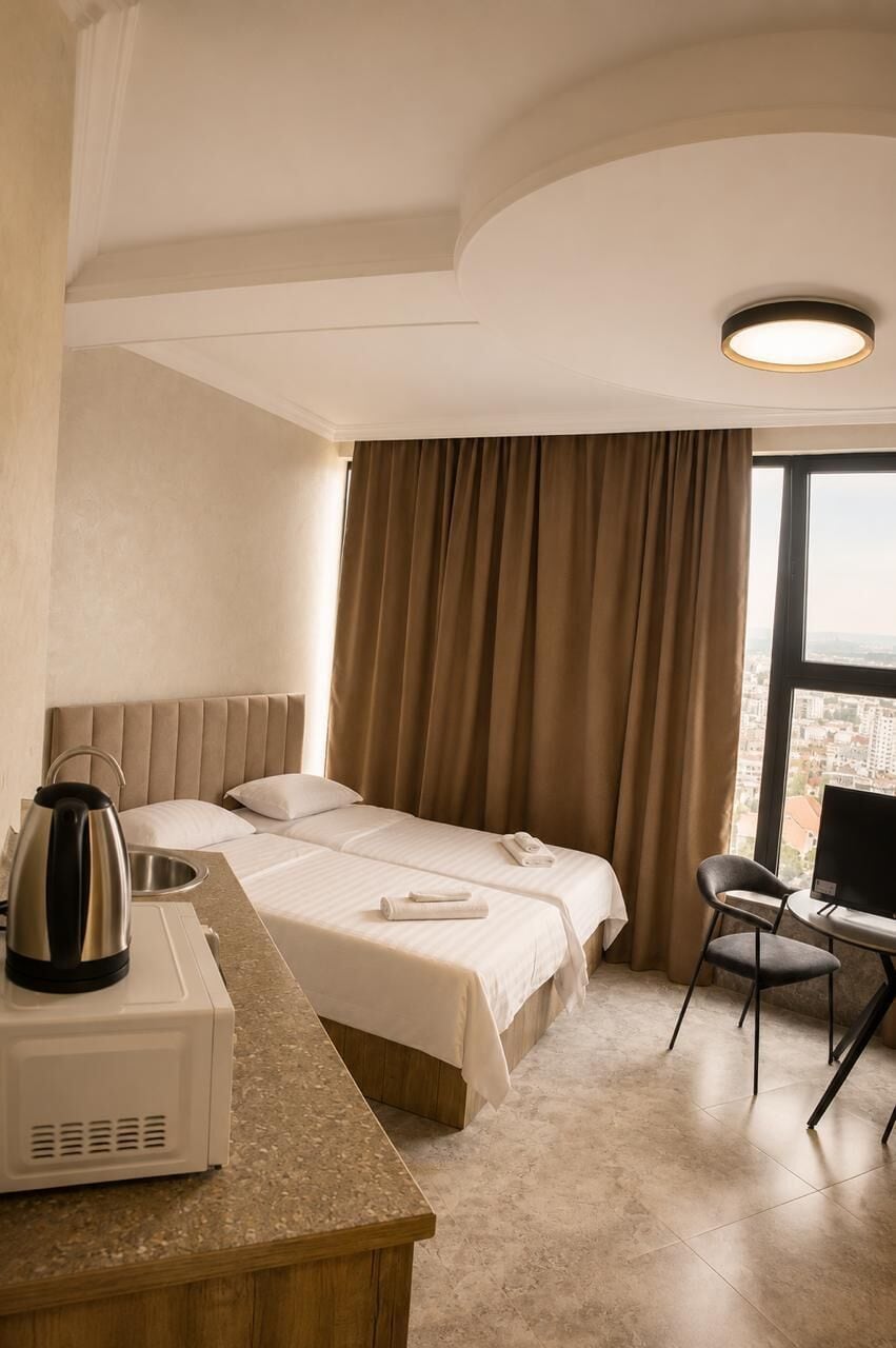 Habitación de hotel con cama, escritorio, silla, cafetera y vista a la ciudad.