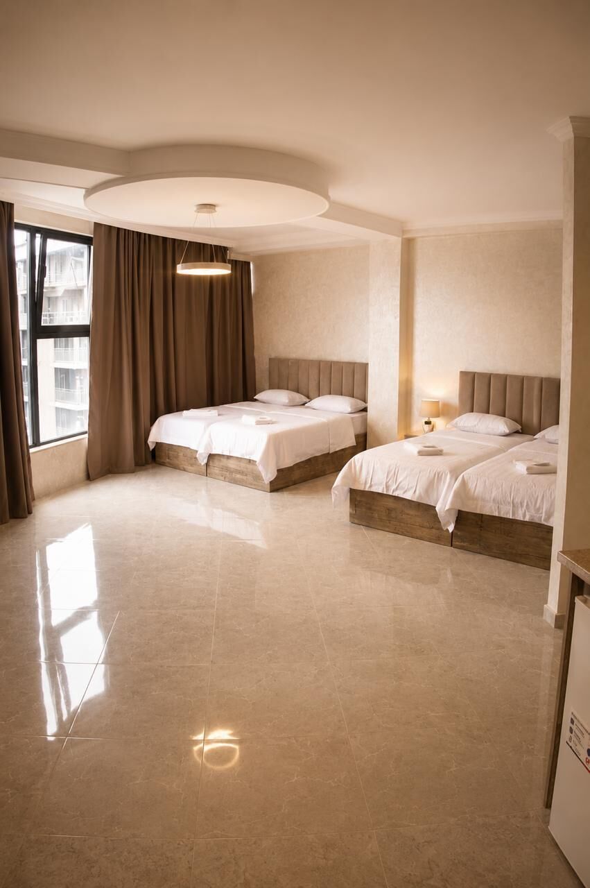 Habitación de hotel con dos camas, un ventanal con cortinas, una lámpara en el techo y suelo de baldosas.