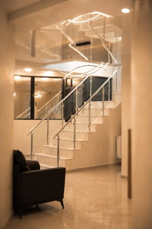 A modern interior with a staircase, a black armchair, and a glass railing. - V E L O R Hotel apartment (Batumi)