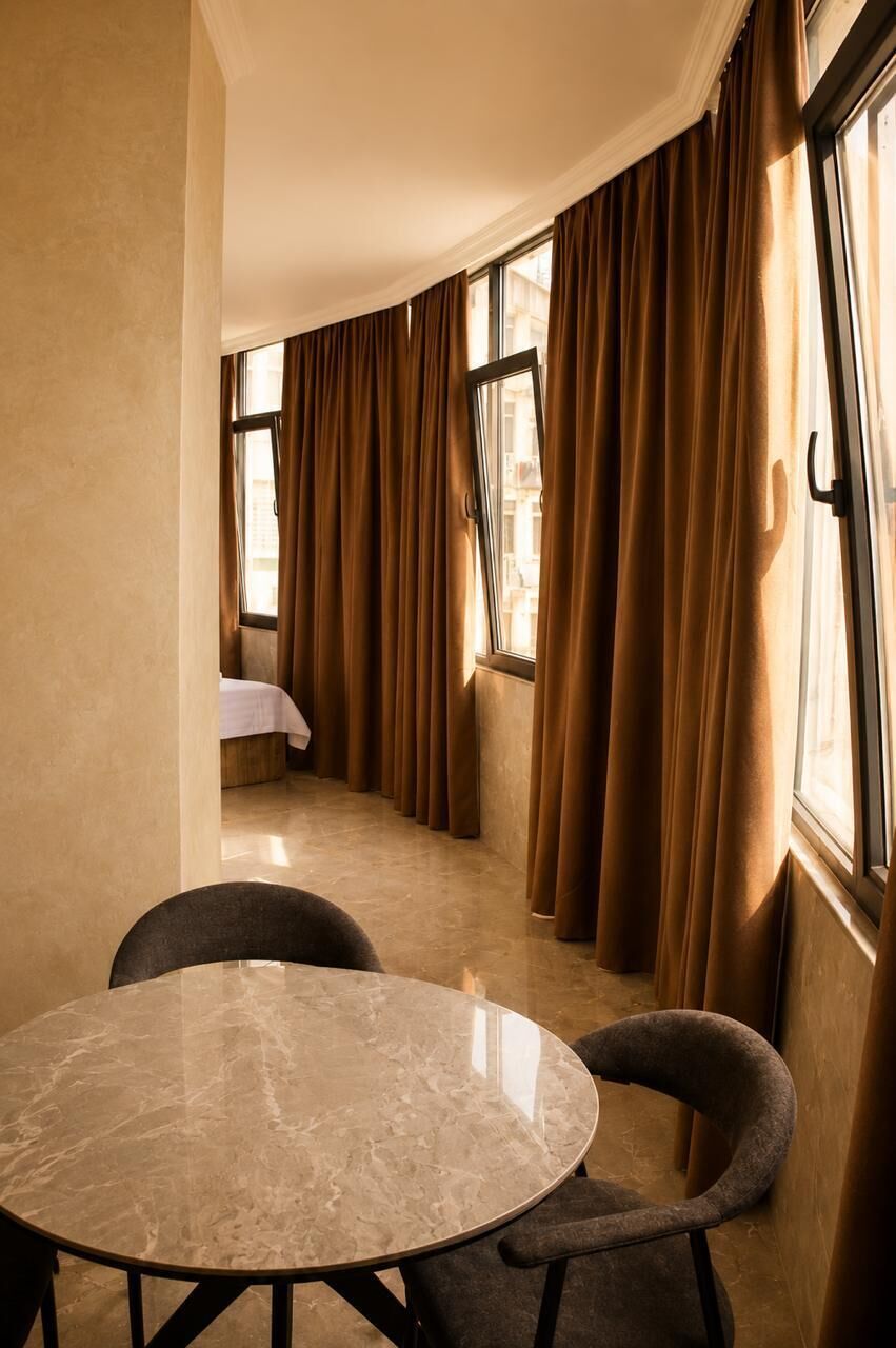 Una habitación de hotel con una mesa redonda de mármol, dos sillas y una cama al fondo.