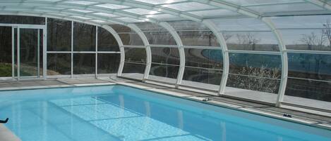 A swimming pool with a glass enclosure, clear water, and a view of the surrounding landscape.