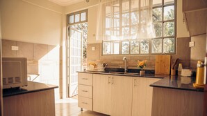 A modern kitchen with wooden cabinets, a black countertop, a sink, and a window with a view of trees. - Lights & Kulture Homes a 2-bedroom apartment for creatives in Arusha Region (Arusha Region)