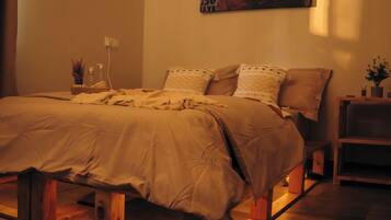 A bedroom with a bed, a nightstand, a wall-mounted painting, and a window casting light on the bed.