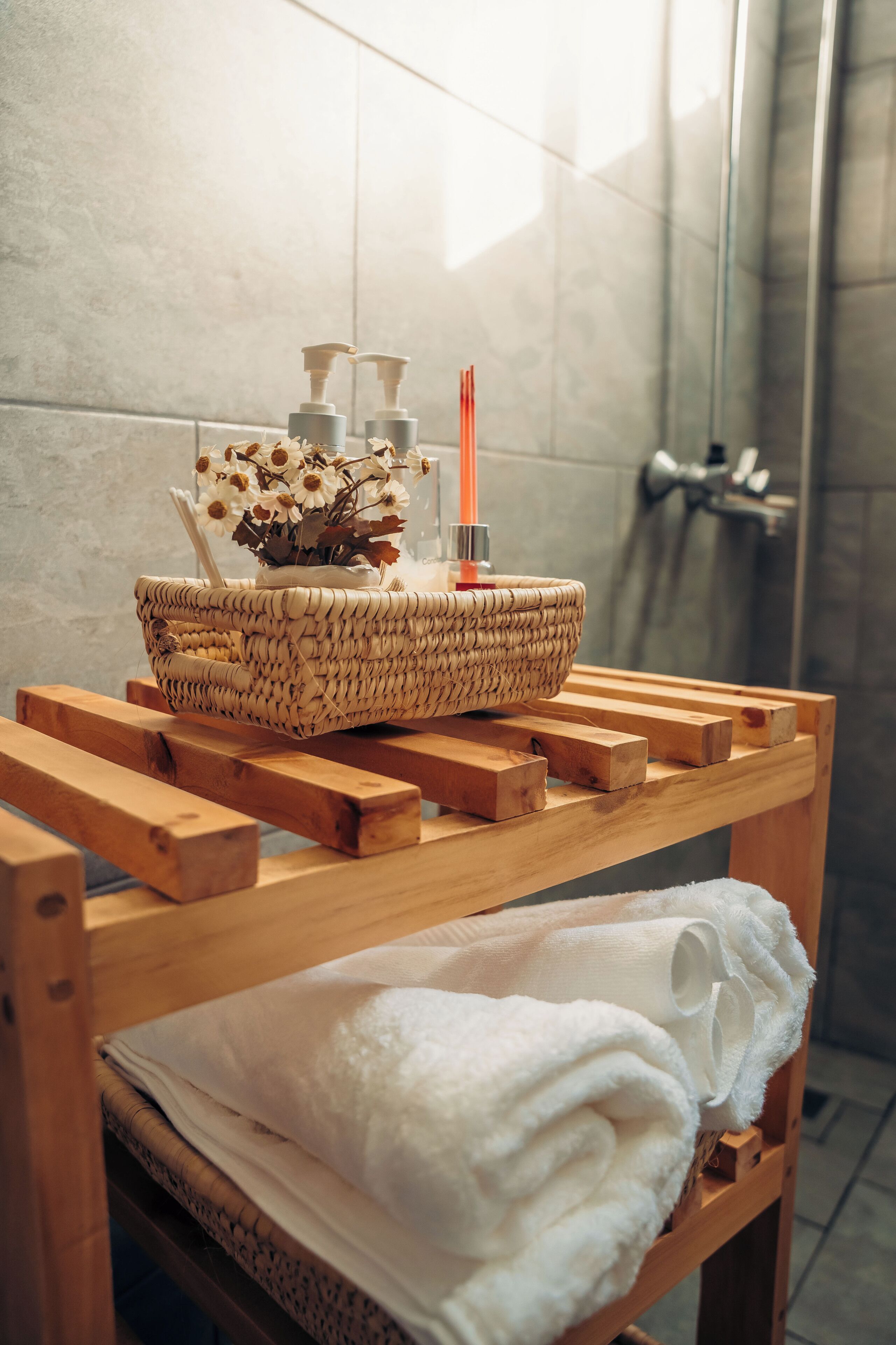Ein Badezimmer mit einer hölzernen Sitzbank, einem gewebten Korb mit Toilettenartikeln und einem Handtuch.