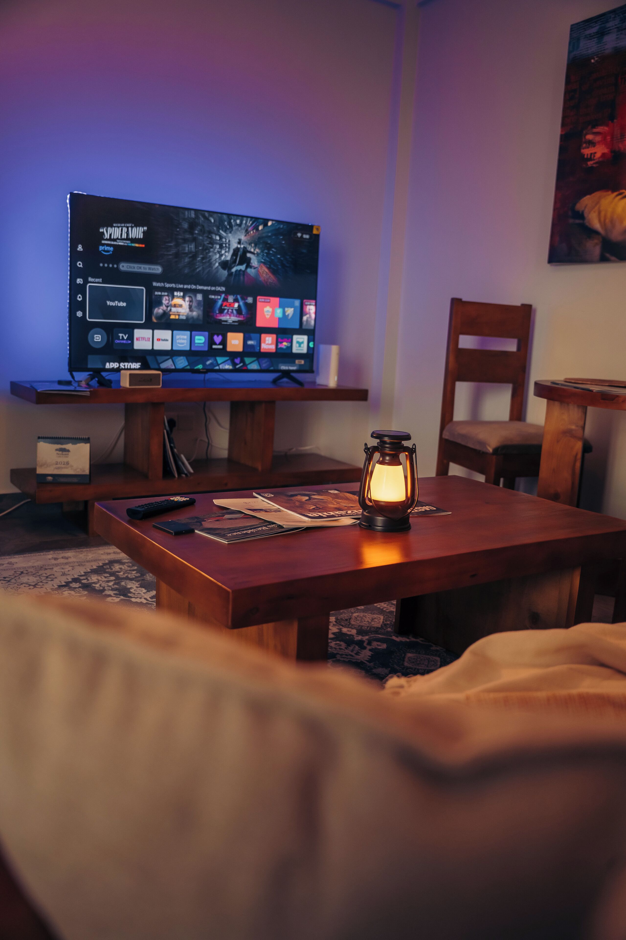 A room with a TV on a wooden stand, a remote control, a lantern, and a chair.