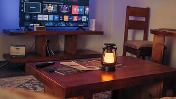 A room with a TV on a wooden stand, a remote control, a lantern, and a chair.