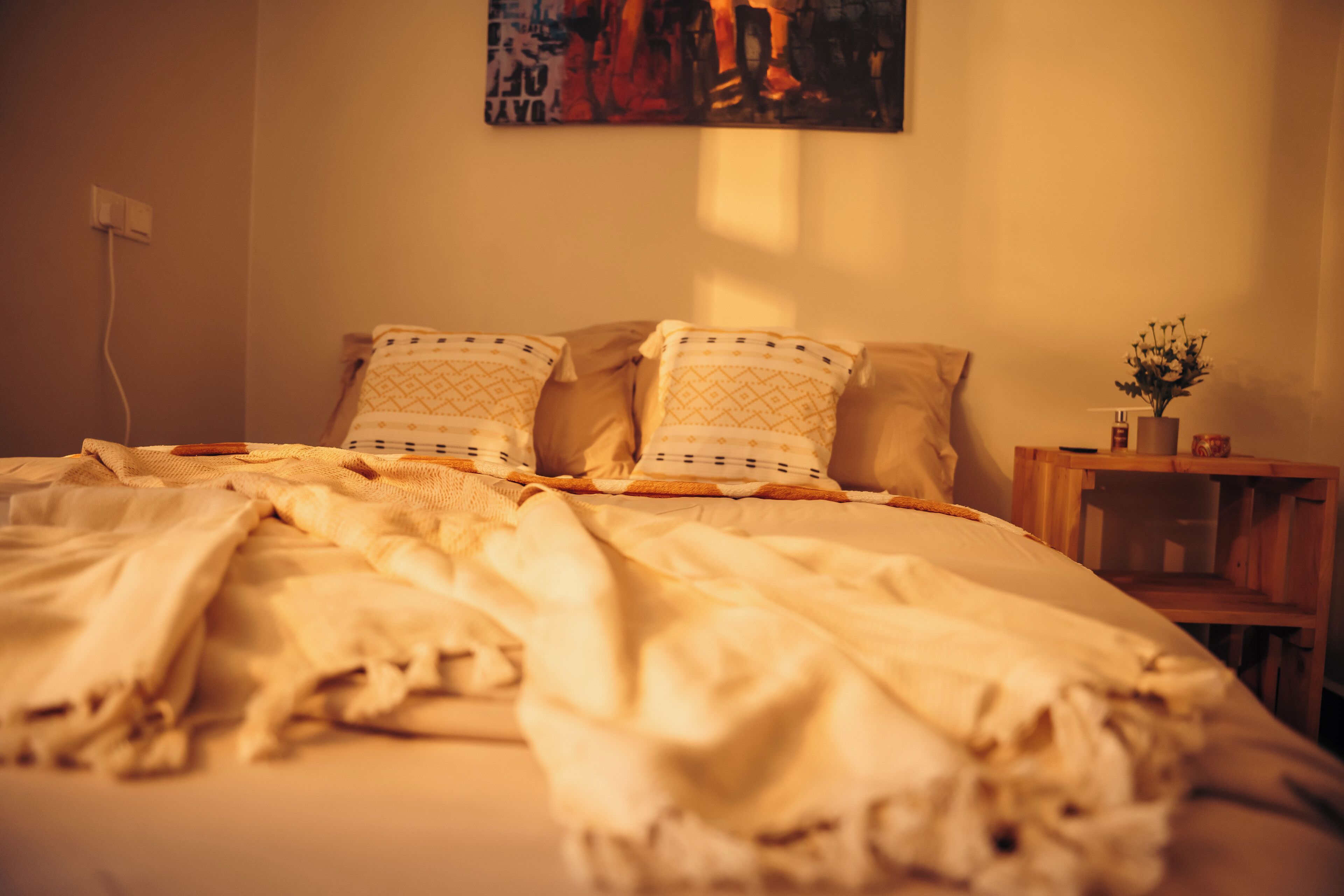 Ein Bett mit einer gemusterten Decke, Kissen und einem Nachttisch mit einer Blumenvase.
