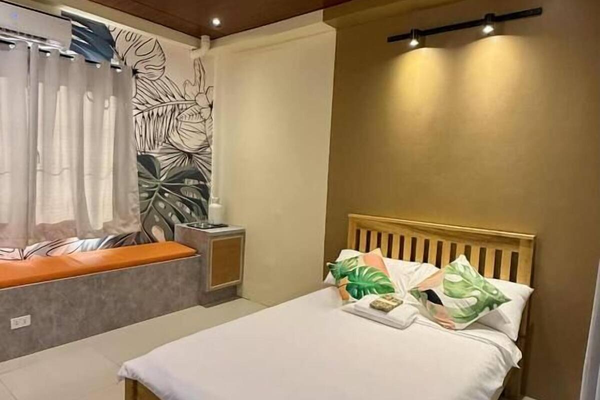 A bedroom with a bed, a bedside table, a wall-mounted shelf, and a ceiling light.