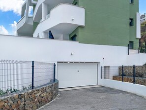 Ein modernes Gebäude mit einer weißen und grünen Fassade, einer weißen Garagentür sowie einer Steinmauer mit einem Metallzaun.