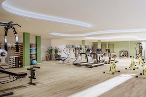 Ein geräumiges Fitnessstudio mit verschiedenen Trainingsgeräten, darunter Laufbänder, Ergometer und Kraftgeräte.