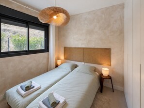 Ein Schlafzimmer mit zwei Betten, einem großen Fenster und einer gewobenen Lampe.