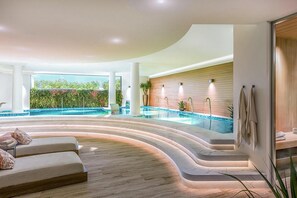Ein moderner Poolbereich im Innenbereich mit einer geschwungenen Sitzecke, einer Holzvertäfelung und Blick auf Grünflächen im Freien.