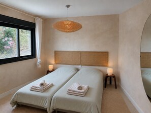 Une chambre avec deux lits, une grande fenêtre, un luminaire en fibres tressées et des lampes de chevet.