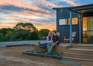 A modern outdoor seating area with a view of the sunset, a small building with a window, and a garden with plants.