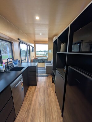Cocina compacta con lavavajillas, lavabo y refrigerador. Hay una ventana que ofrece vistas al exterior.