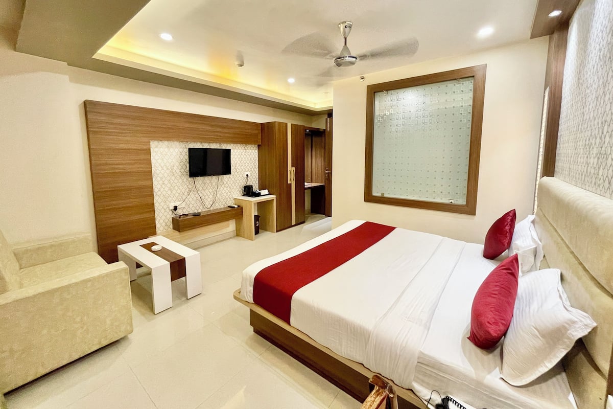 A modern bedroom with a large bed, a TV mounted on the wall, a ceiling fan, and a window with frosted glass.
