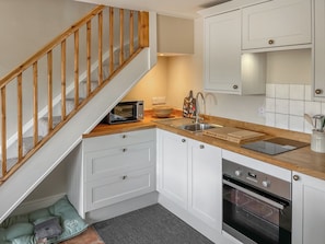 A compact kitchen with white cabinets, a wooden staircase, a microwave, a sink, and an oven. - The Cartshed - UK50426 (Malton)