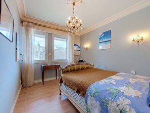 A bedroom with a bed, a nightstand, a chandelier, a window with curtains, and wall-mounted lights. - Hotel de Ville by Interhome (Perros Guirec)