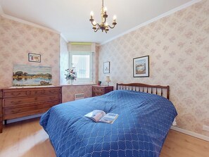 Ein Schlafzimmer mit Bett, Kommode, Fenster und Wandbildern.