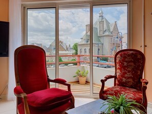 A room with two red upholstered chairs, a small table, and a view of a historic building through a large window. - Hotel de Ville by Interhome (Perros Guirec)