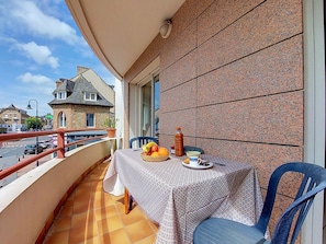 Un balcon avec une table préparée pour le petit-déjeuner, une chaise et un pot de fleurs.