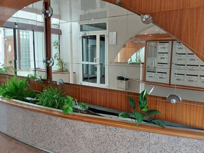 A reception area with a glass partition, a wooden reception desk, a trash bin, and a plant. - Hotel de Ville by Interhome (Perros Guirec)
