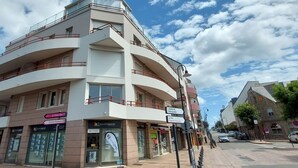 Monikerroksinen rakennus, jossa on parvekkeita, ja sen julkisivussa on kyltti, jossa lukee »SQUARE HABITAT». Kadulla on autoja ja jalankulkijoita.