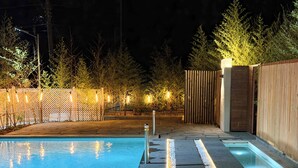 Una piscina con borde de baldosas, rodeada de un cerco de madera y árboles.