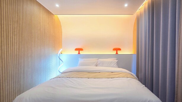 Una habitación de hotel moderna con una cama, dos lámparas de noche y un panel de pared de madera.