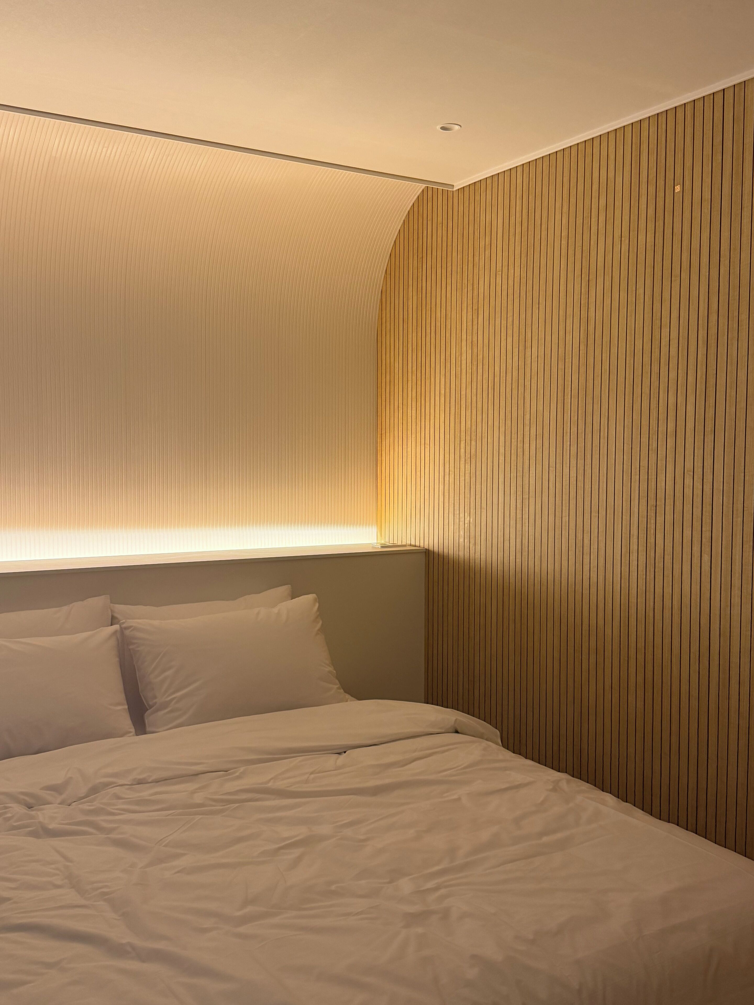A bedroom with a bed, pillows, a headboard, and a wall with vertical wooden slats.
