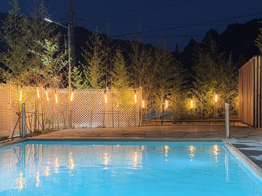 A swimming pool with a wooden deck and a fence with lights.