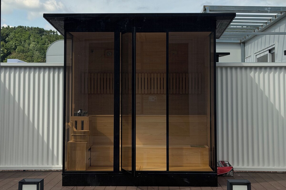 A modern outdoor structure with a glass door, a wooden interior, and a pool area.