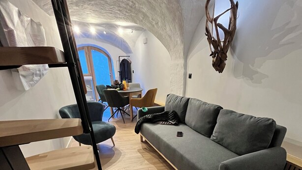 Un interior moderno con un sofá gris, una mesa de centro de madera, una escalera y un comedor con sillas y una mesa.