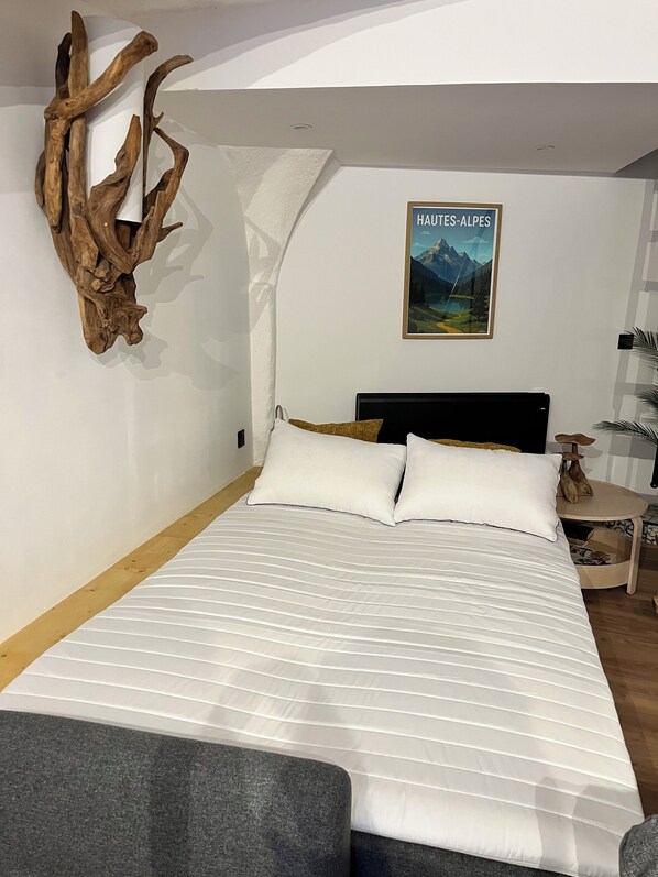 A bedroom with a large bed, a wooden wall decor, a framed picture, and a bedside table.