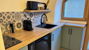 Una cocina compacta con encimera de madera, una cafetera negra, un fregadero y un lavavajillas.