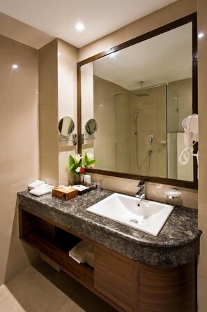 Un baño moderno con encimera de granito, un lavabo blanco, un espejo grande y una ducha con cerramiento de vidrio.