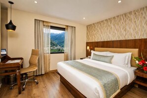 Habitación de hotel con una cama grande, un escritorio con una computadora y vista a un paisaje montañoso a través de la ventana.