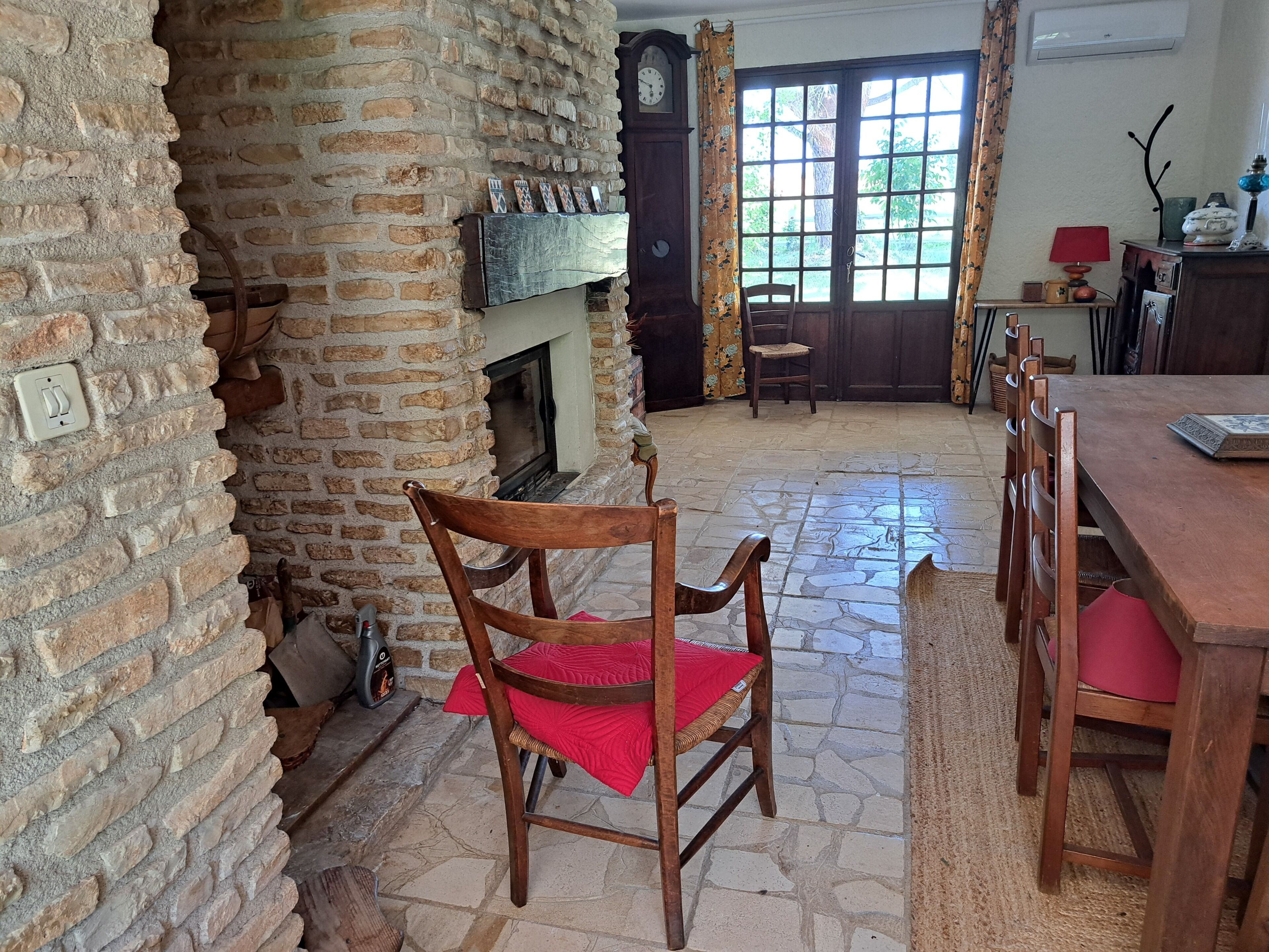 A room with a fireplace, a dining table, chairs, and a large window.