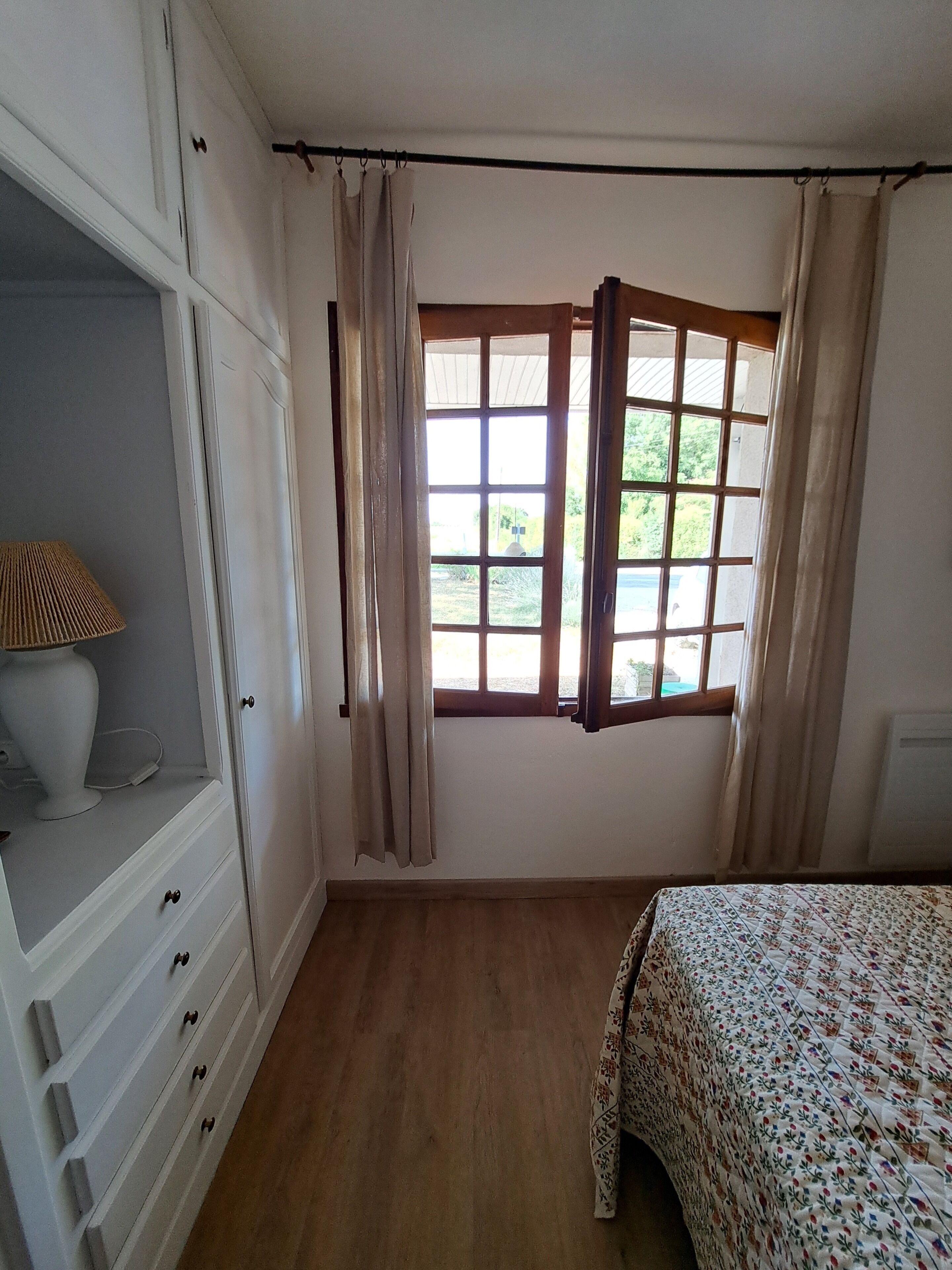 A bedroom with a bed, a dresser, a window with curtains, and a lamp.