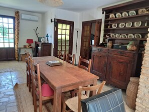 Un coin repas comprenant une table en bois, des chaises, un banc, une lampe, une étagère avec des assiettes décoratives et un panier en osier.