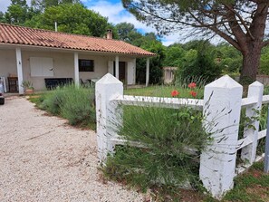 Une maison avec un toit en tuiles, une allée en gravier et une clôture blanche en bois.