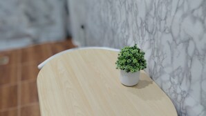 A small round table with a potted plant, white metal chair, and a marble wall in the background. - ROW HOUSE WITH PRIVATE POOL, Corner Townhouse with Private Pool (หัวหิน)