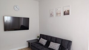 A modern living room with a dark grey sofa, a flat-screen TV, a small table, and three framed pictures on the wall. - ROW HOUSE WITH PRIVATE POOL, Corner Townhouse with Private Pool (หัวหิน)
