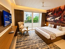 A hotel room with a bed, a chair, a small table, a TV, and a balcony with a view.