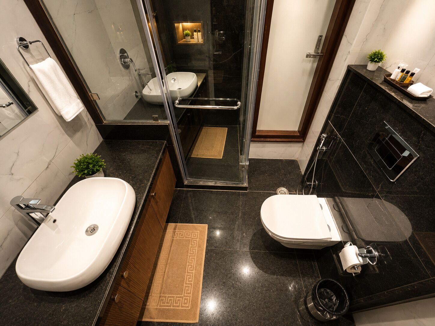 A modern bathroom with a large white sink, a separate toilet, a glass-enclosed shower, and a dark marble countertop.
