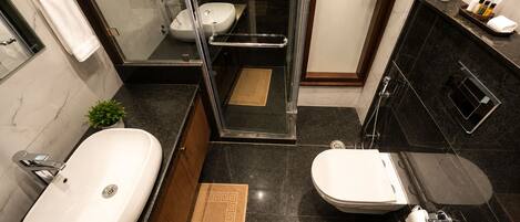 A modern bathroom with a large white sink, a separate toilet, a glass-enclosed shower, and a dark marble countertop.