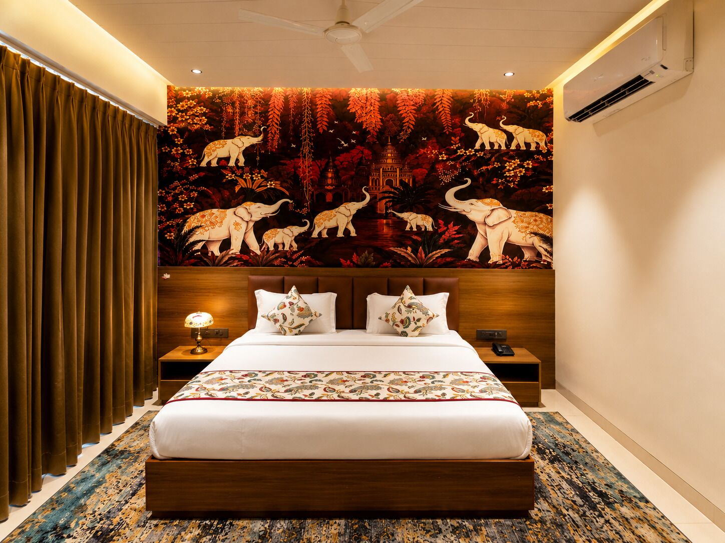A hotel room with a large bed, a nightstand, a lamp, and a wall mural of elephants.