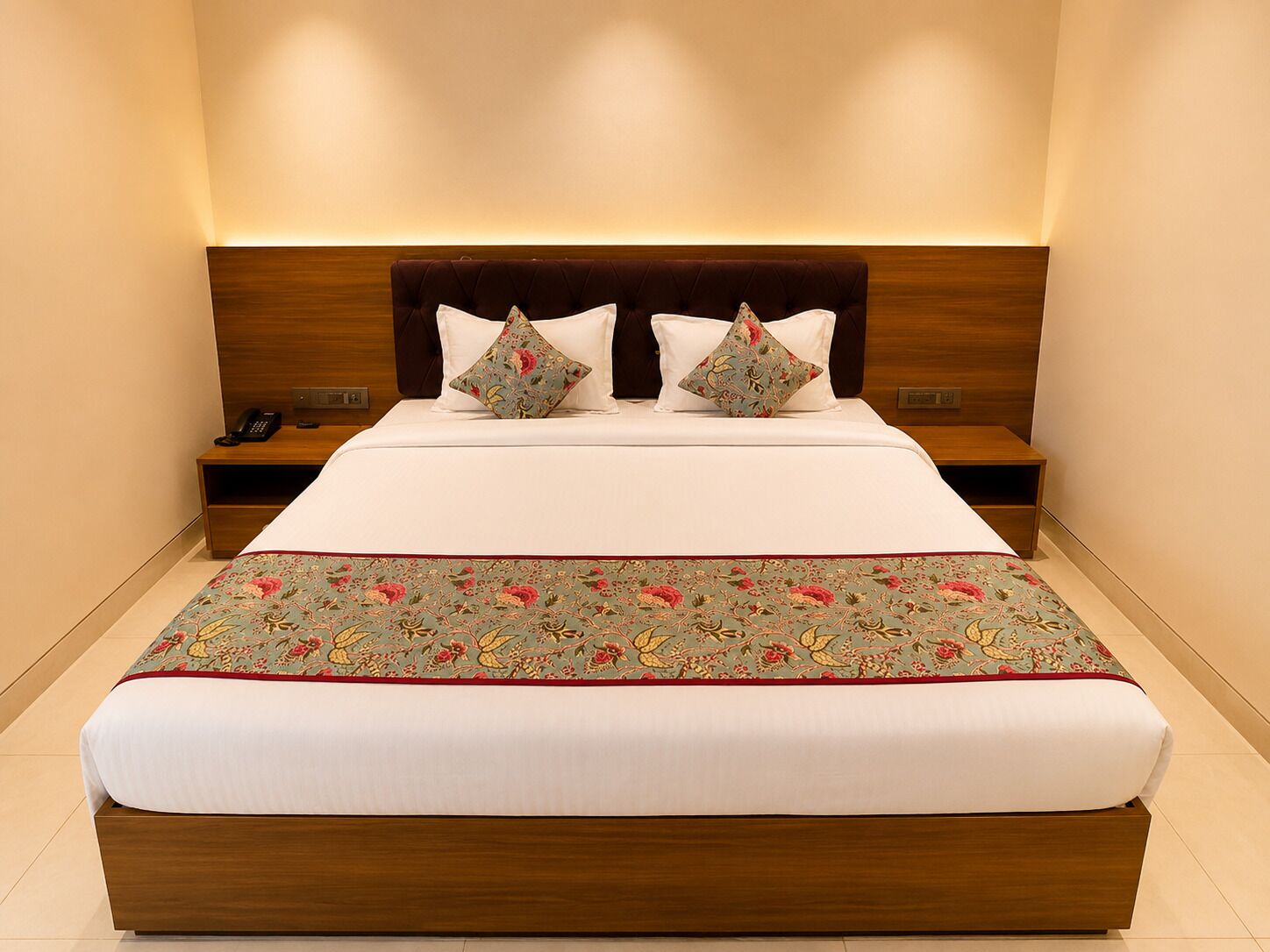 Un letto rifatto con cura, con una coperta a fiori, due cuscini e una testiera in legno.